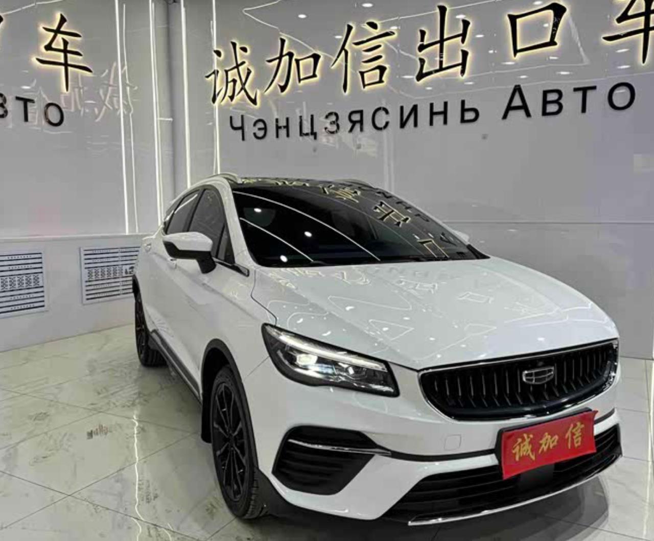 Белый кроссовер Geely в шоуруме китайского экспортного дилера: на стене вывеска «Чэнцзясинь АВТО», на решётке — красная табличка дилера