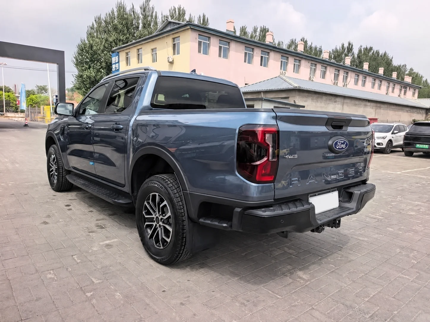Пикап Ford Ranger сине-серого цвета сзади слева на асфальтированной площадке: борт кузова, задний фонарь, подножка и надпись RANGER на откидном борте